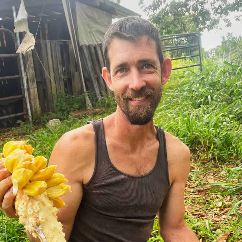 Mickey from Rainbow Bridge Hawaii holding freshly harvested tropical fruit in the community garden on Hawai‘i Island.