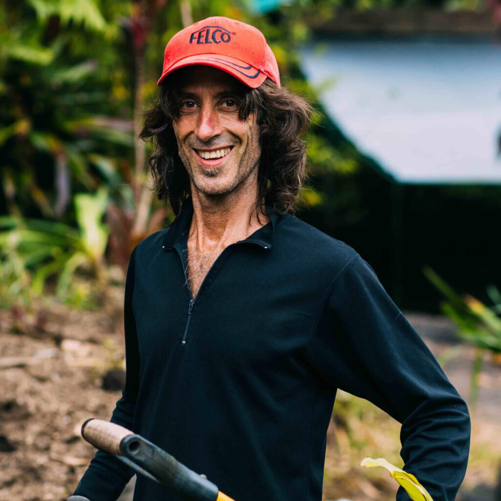 Rainbow Bridge Hawaii community member gardening during a volunteer work day, holding a shovel and plant roots