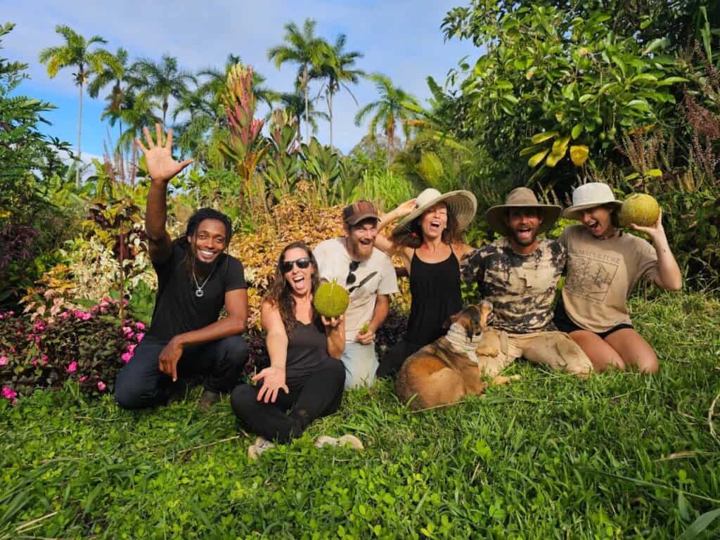Volunteers celebrating a garden work day at Rainbow Bridge Hawaii, surrounded by tropical plants and fresh fruit