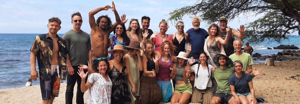 Group of Lucid Dreams Retreat participants gathered on a beach in Hawaii, smiling and waving near the ocean.