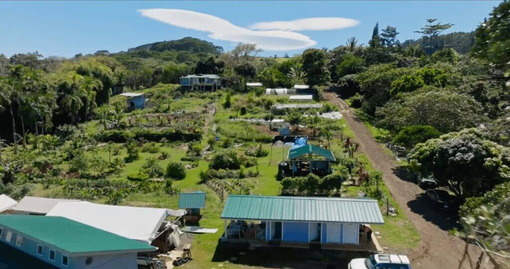 Aerial view of Rainbow Bridge Hawaii with gardens, buildings, tropical trees, and green hills under a blue sky.