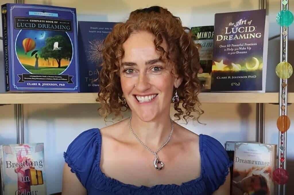 Dr. Claire Johnson, Lucid dreaming teacher smiling in front of books about lucid dreaming and dreamwork for the Healing Dreams Retreat.