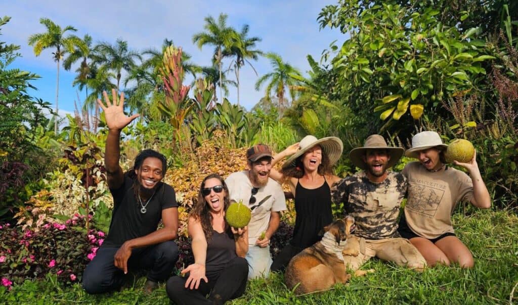Volunteers celebrating a garden work day at Rainbow Bridge Hawaii, surrounded by tropical plants and fresh fruit