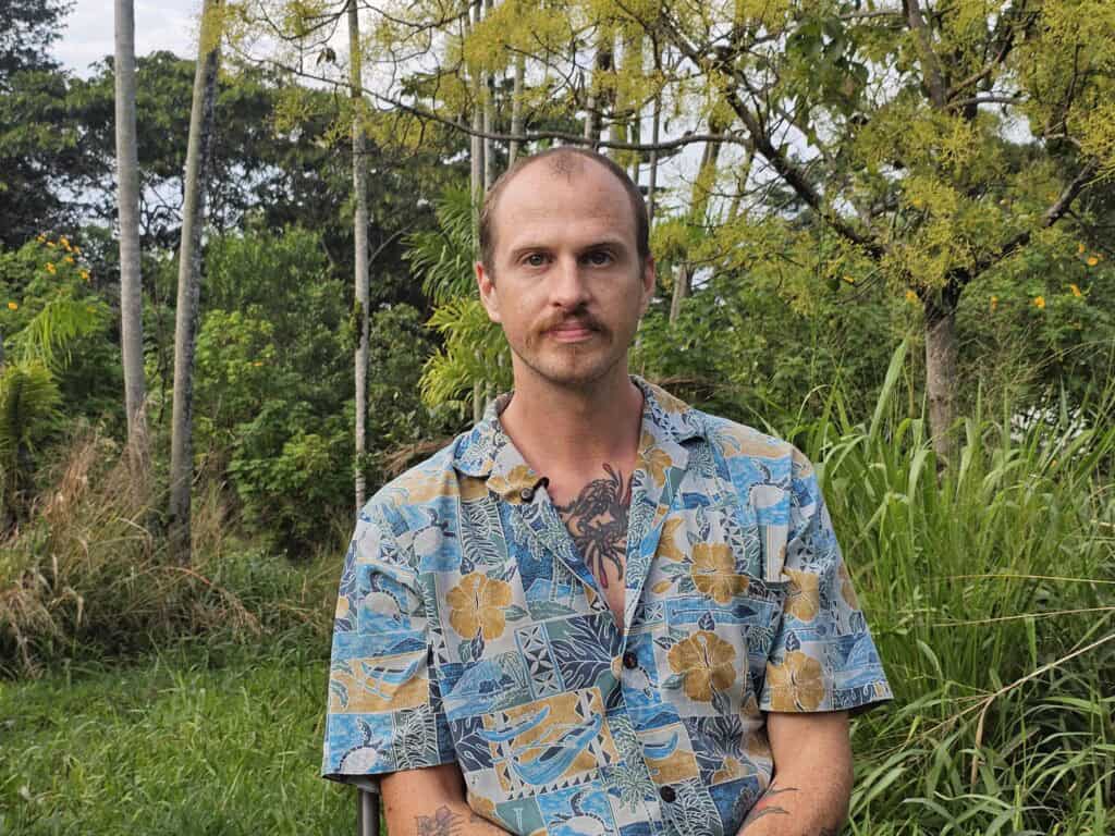 Joshua Houston sitting outdoors in a tropical setting during his Rainbow Bridge Hawaii worktrade experience.