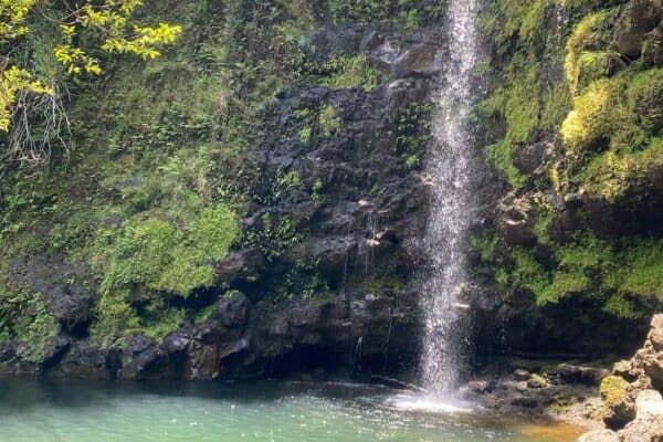 Noelani Waterfall and natural pool on the land at Rainbow Bridge Hawaii, surrounded by lush tropical greenery