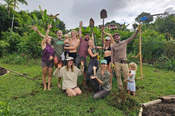 Community members smiling and raising garden tools during a garden work day in a tropical Hawaii garden