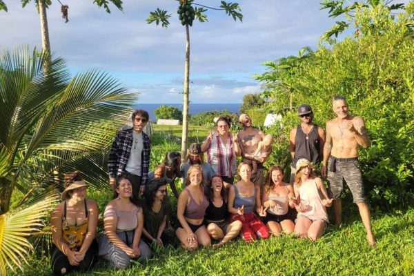 Group of community members sitting and standing together on grass in a tropical Hawaii garden with palm trees and ocean in the background