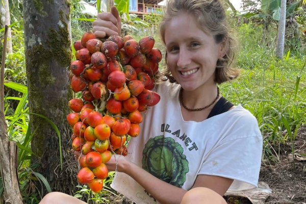 Community member holding a fresh harvest of tropical fruit (peach palms) at Rainbow Bridge Hawaii, surrounded by lush garden plants