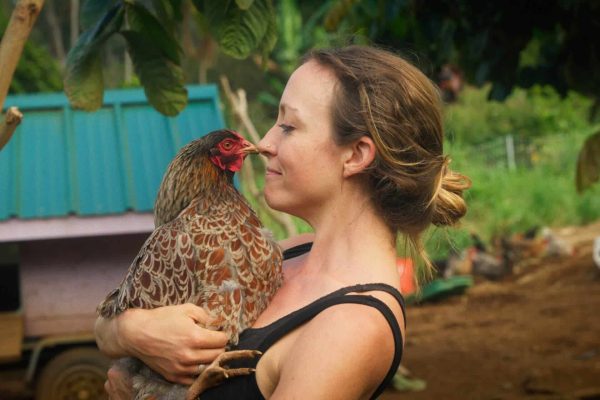 Woman holding a rescued hen named BT (Bushy Tail) at Rainbow Bridge Hawaii animal sanctuary.
